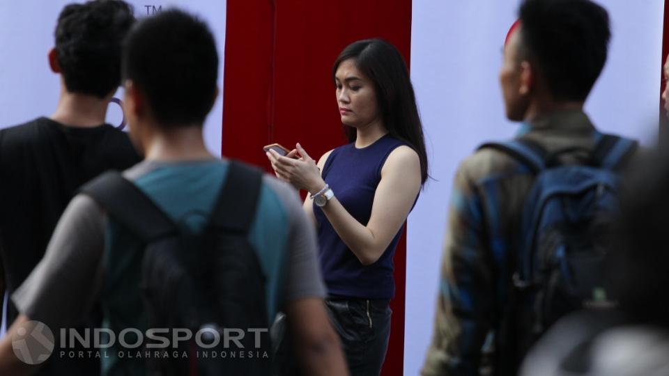 Wanita cantik berambut panjang ini asik memainkan gadget di area pertandingan.
