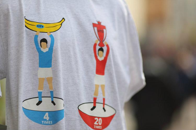 Sebuah baju yang memperlihatkan perbedaan raihan trofi Liga Primer Inggris antara MU dan Man City. Copyright: Matthew Ashton - AMA/Getty Images