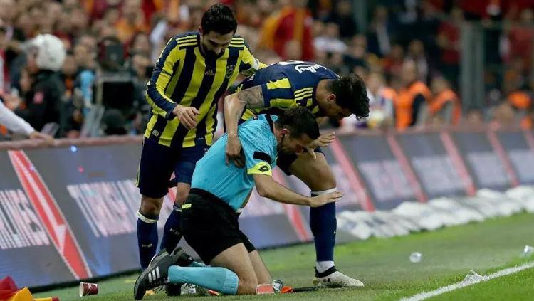 Dua pemain Fenerbahce membantu wasit yang tengah dilempari minuman oleh suporter. Copyright: thesun.co.uk