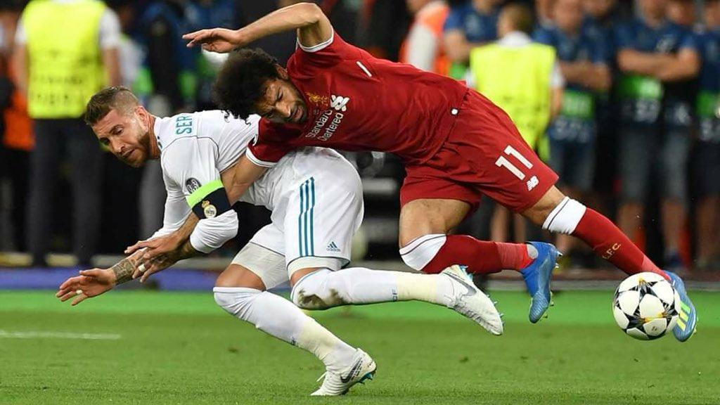 Sergio Ramos meraik tangan Mohamed Salah. - INDOSPORT