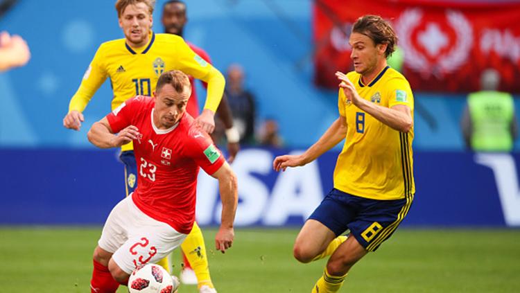 Xherdan Shaqiri berusaha melewati dua pemain Swedia sambil membawa bola.