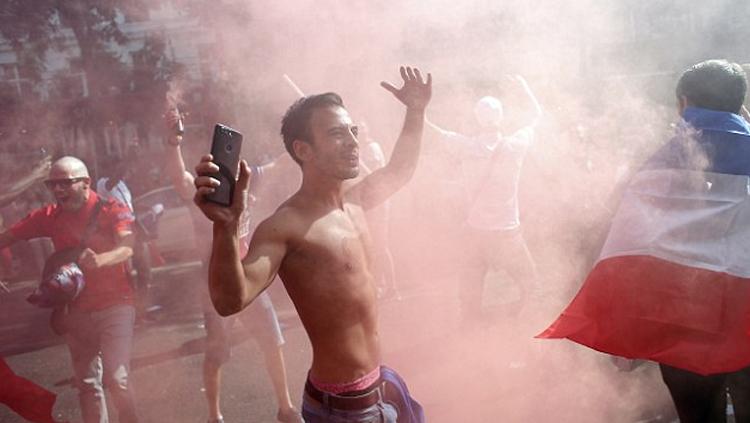 Seorang pendukung Perancis merayakan di tengah-tengah flare setelah negaranya juara Piala Dunia 2018.