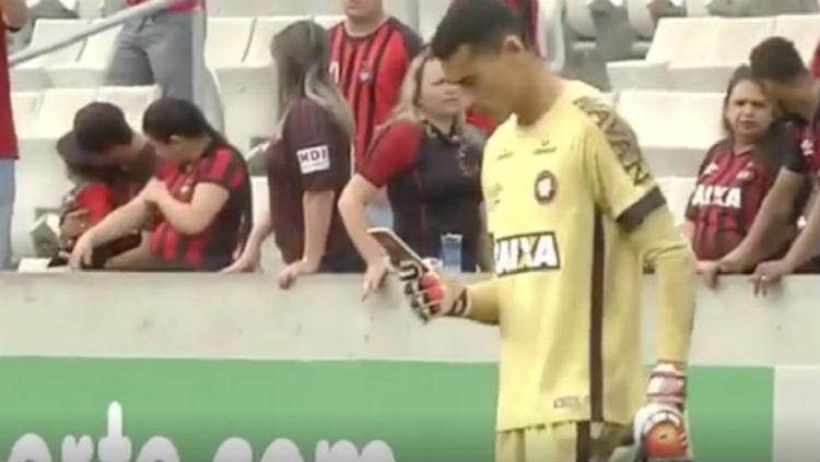 Santos, kiper Atletico Paranaense, memainkan telepon genggam saat pertandingan.
