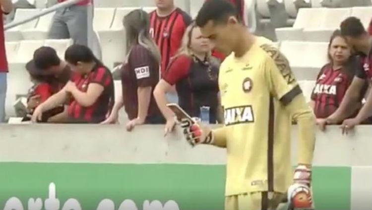 Santos, kiper Atletico Paranaense, memainkan telepon genggam saat pertandingan. - INDOSPORT