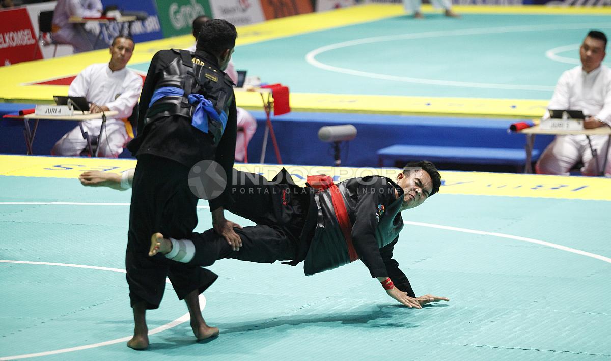 Pesilat Indonesia, Komang Adi Putra (sabuk merah) melawan Pesilat Timor Leste (sabuk biru) pada babak 16 besar Kelas E Putra 65 kg-70kg di Padepokan Pencak Silat TMII, Rabu (23/08/18). Komang menang telak 5 poin atas lawannya.