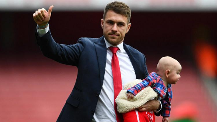 Aaron Ramsey menggendong putranya saat berpamitan usai laga Arsenal vs Brighton di Emirates Stadion, Minggu (05/05/19). - INDOSPORT