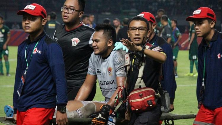 Kiper Kalteng Putra, Dimas Galih, ditandu ke luar lapangan usai terkena lemparan botol dari suporter di Stadion GBT. Copyright: Fitra Herdian/INDOSPORT