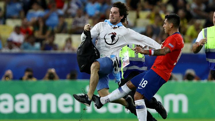 Pemain Chile Gonzalo Jara, menekel seorang pitch invader dalam laga melawan Uruguay di Copa America, Selasa (25/06/19).