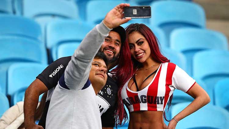 Suporter seksi Timnas Paraguay menerima ajakan foto bareng dua suporter laki-laki di laga perempatfinal Copa America.
