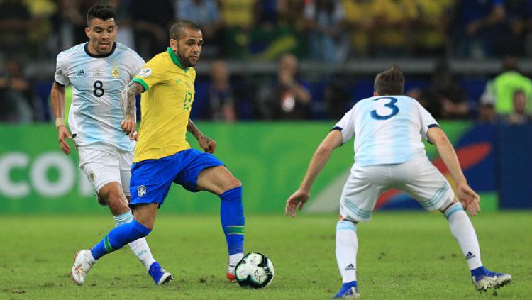 Dani Alves menggiring bola sambil dikawal ketat oleh pemain Argentina. Copyright: Getty Images