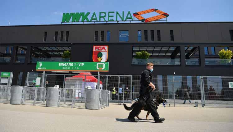 Seorang polisi dan anjing penjaga berpatroli di luar WWK-Arena dalam laga Bundesliga antara FC Augsburg vs VFL Wolfsburg, Sabtu (16/05/20).