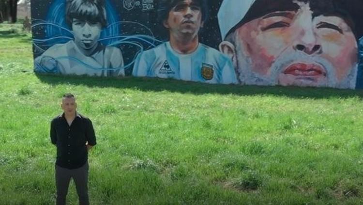 Pelatih sepak bola asal Argentina, Carlos Alberto Gomez, ketika berfoto di depan mural Diego Maradona. - INDOSPORT