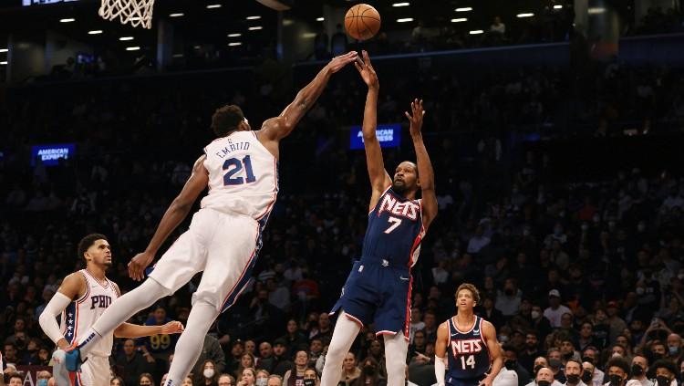 Kevin Durant (Nets) melepaskan tembakan 3 poin yang coba dihalau Joel Embiid (Sixers), Jumat (17/12/21).