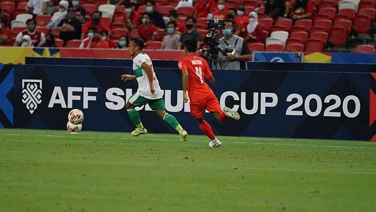 Irfan Jaya lebih cepat dari pemain Singapura untuk mendapatkan bola pada laga Piala AFF 2020 semifinal leg 1