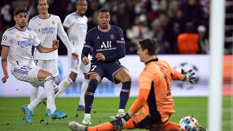 Pemain PSG, Kylian Mbappe saat menceploskan bola ke gawang Real Madrid yang dikawal Thibaut Courtois. - INDOSPORT