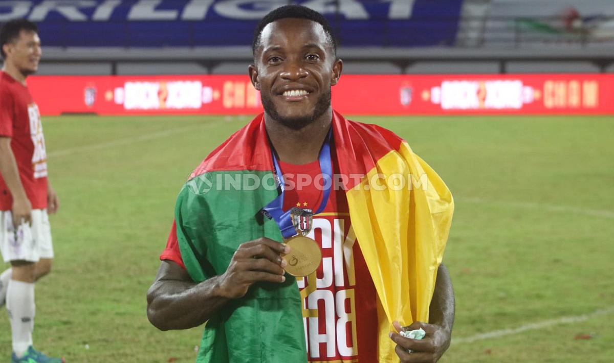 Privat Mbarga dengan medali Liga 1 2021/2022 dan bendera negara Kamerun.