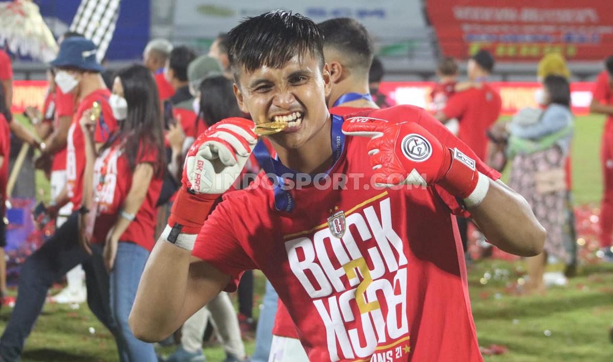 Kiper muda Bali United, Rakasurya Handika menggigit medali gelar juara Liga 1 2021/2022.