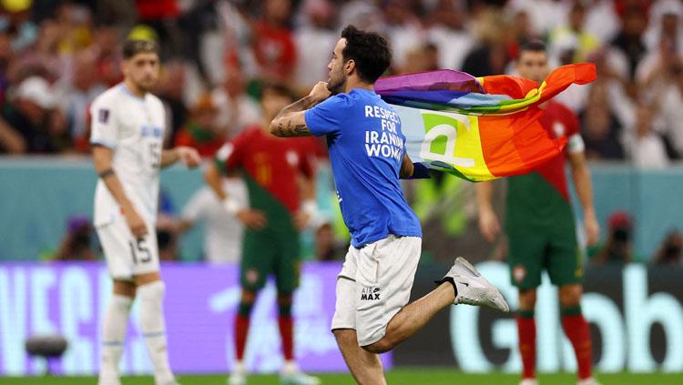 Seorang tak dikenal berlari sambil mengibarkan bendera pelangi di laga kedua Grup H Piala Dunia antara Portugal vs Uruguay (Foto: REUTERS/Kai Pfaffenbach).