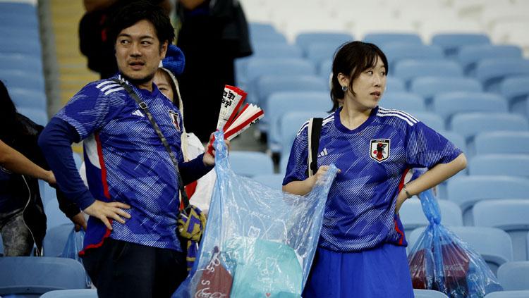 Fans Jepang membersihkan tribun penonton Stadion Al Janoub usai pertandingan melawan Kroasia di babak 16 besar Piala Dunia 2022 (Foto:  REUTERS/John Sibley). - INDOSPORT