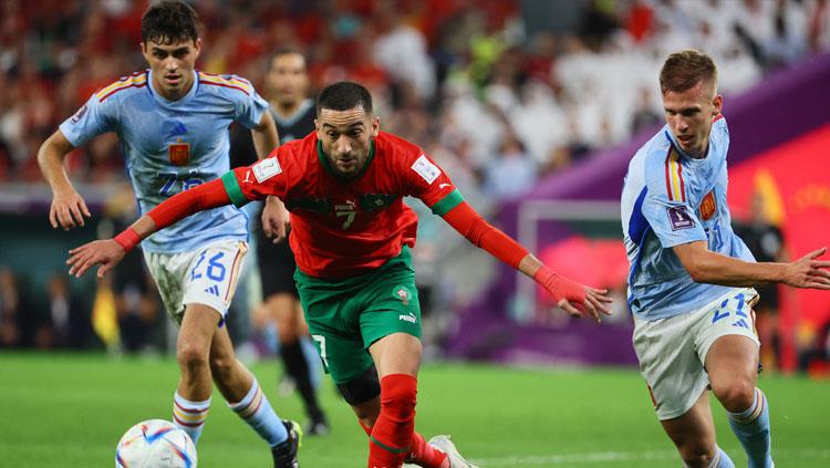 Pemain bintang Maroko, Hakim Ziyech (tengah) dijaga ketat oleh pemain Spanyol, Dani Olmo (kanan) dalam pertandingan babak 16 besar Piala Dunia 2022 (Foto: REUTERS/Wolfgang Rattay). - INDOSPORT