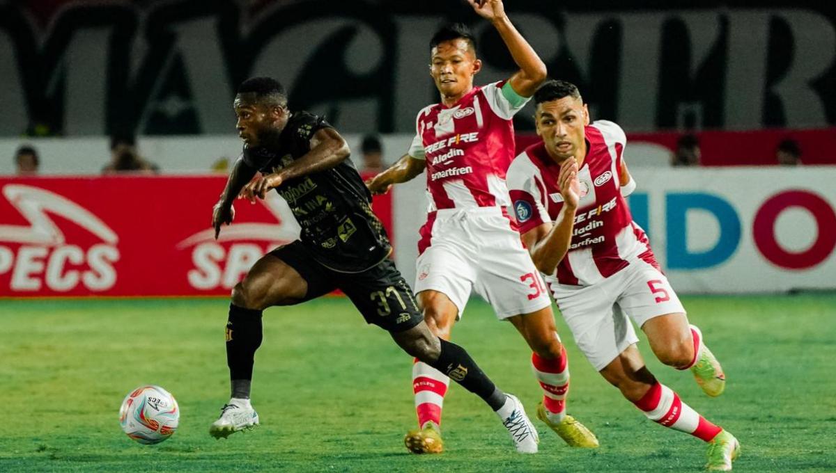 Dua bek Persis Solo berjibaku menghentikan pergerakan pemain Bali United, Privat Mbarga pada laga Liga 1 2023/2024 pekan kesembilan di stadion Manahan, Sabtu (19/08/23). - INDOSPORT