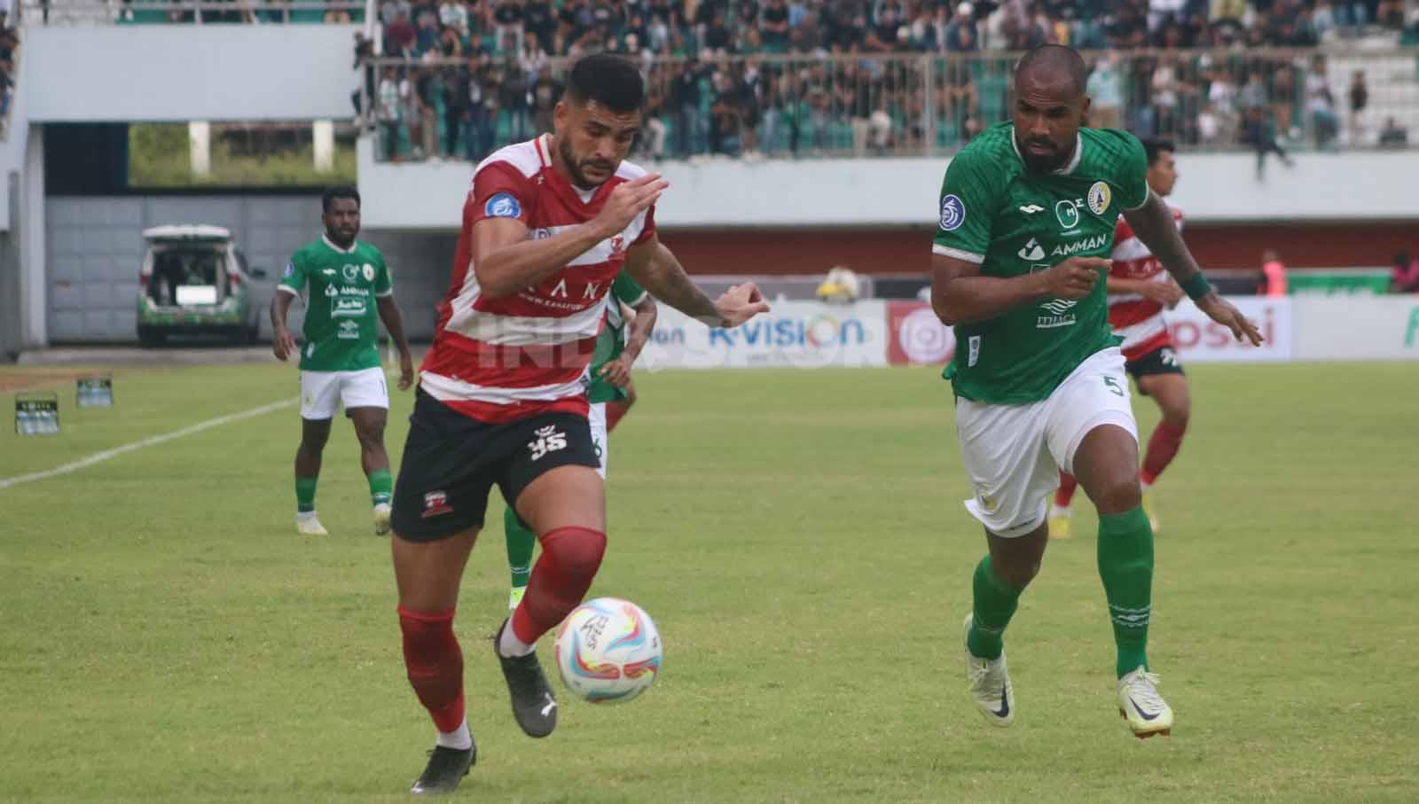 Penyerang Madura United, Junior Brandao, menggiring bola dengan dibayangi bek PSS, Thales Lira,  dalam laga pekan ke-13 Liga 1 2023-2024 di Stadion Maguwoharjo, Minggu (24/9/23).