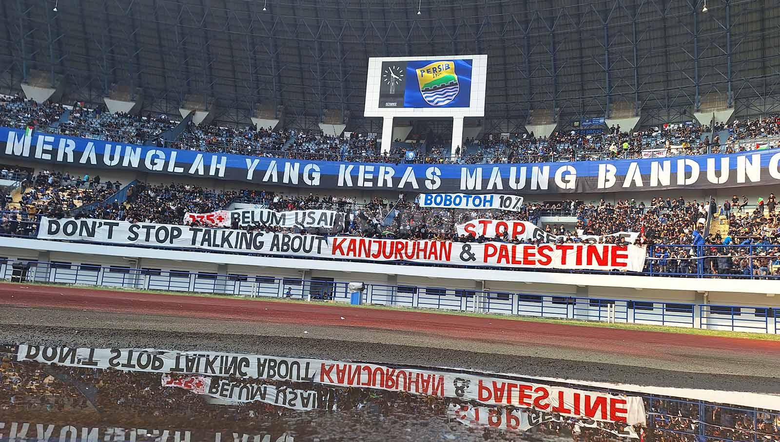 Bobotoh di tribun utara membentangakan spanduk terkait tragedi Kanjuruhan dan Palestina, pada pertandingan Persib vs Arema FC Liga 1 2023-2024 di Stadion GBLA, Kota Bandung, Rabu (08/11/23).