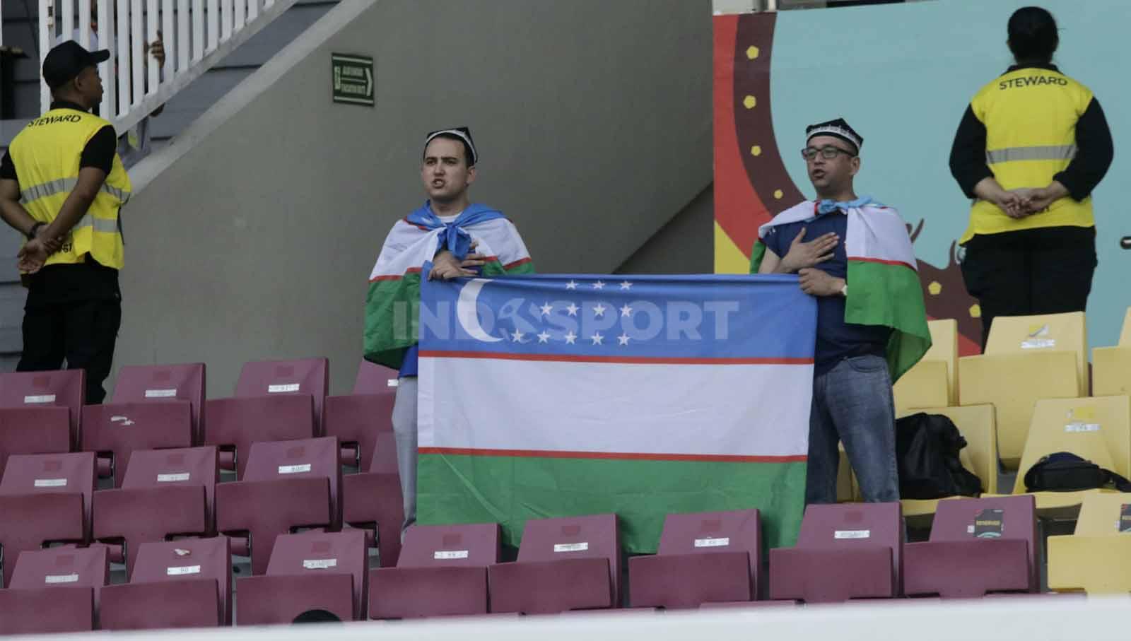Dua suporter Uzbekistan saat mengibarkan bendera negaranya  dalam pertandingan Piala Dunia U-17 2023 grup B antara Mali U-17 melawan Uzbekistan U-17, Jumat (10/11/23). Nofik Lukman Hakim/INDOSPORT