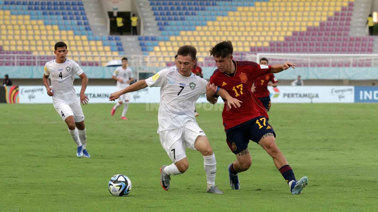 Winger Uzbekistan, Lazizbek Mirzaev, berduel dengan bek Spanyol, Oscar Mesa, dalam pertandingan fase grup B Piala Dunia U-17 2023 di Stadion Manahan Solo, Kamis (16/11/23). (Foto: Nofik Lukman Hakim/INDOSPORT)