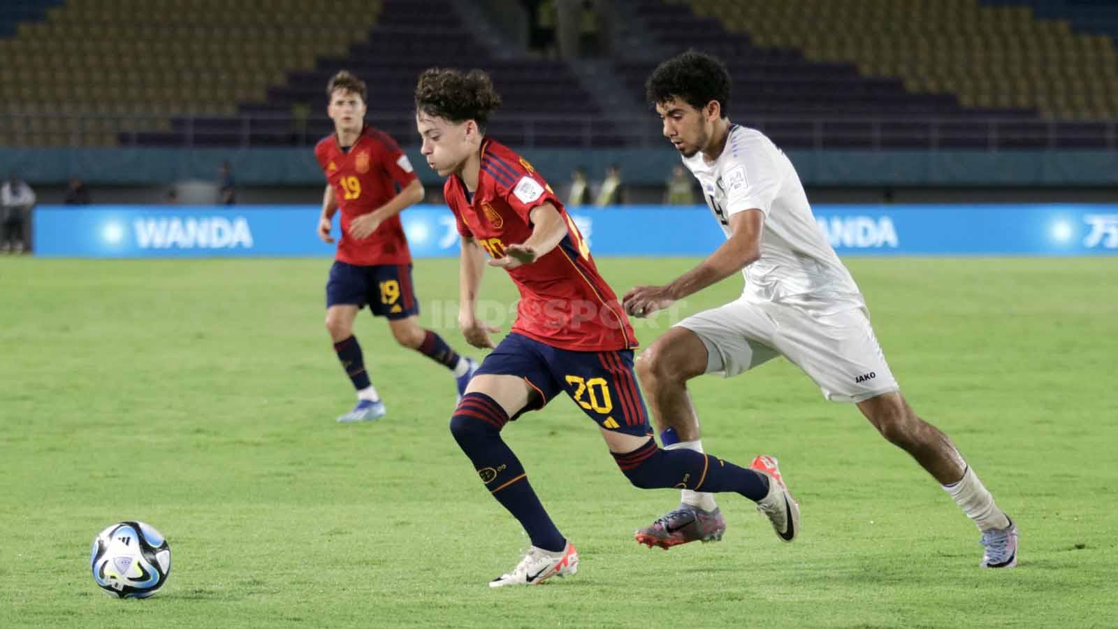 Penyerang Uzbekistan, Amirbek Saidov, berusaha merebut bola yang dikuasai gelandang Spanyol, Iago Paulo,  dalam pertandingan fase grup B Piala Dunia U-17 2023 di Stadion Manahan Solo, Kamis (16/11/23). (Foto: Nofik Lukman Hakim/INDOSPORT)