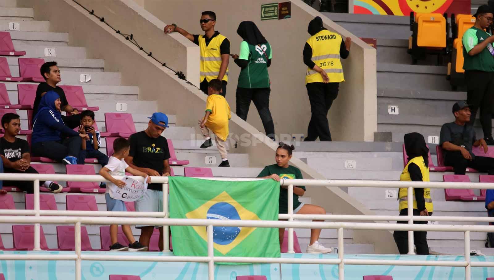 Bek Persis Solo, Jaimerson Xavier, bersama kedua anaknya saat memasang bendera Brasil dalam pertandingan babak 16 besar Piala Dunia U-17 2023 di Stadion Manahan Solo, Senin (20/11/23). (Foto: Nofik Lukman Hakim/INDOSPORT)