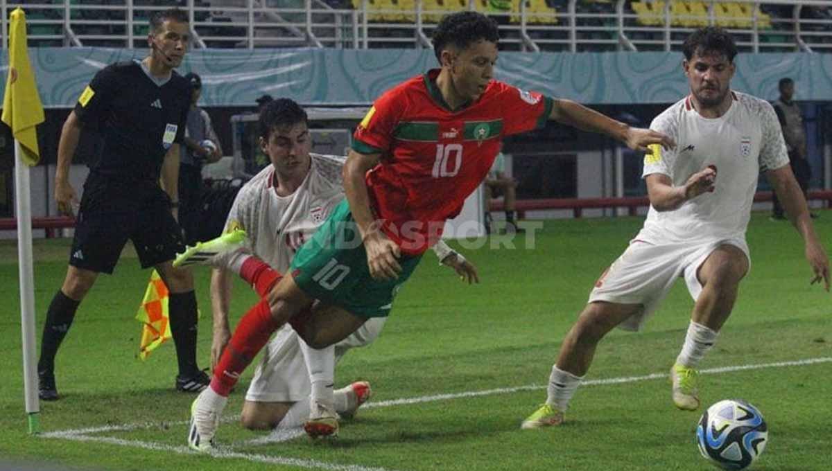 Duel ketat pemain Maroko Imran Nazih diadang dua pemain Iran di laga babak 16 besar Piala Dunia U-17 2023 di Stadion Gelora Bung Tomo, Surabaya, Selasa (21/11/23). (Foto: Fitra Herdian/INDOSPORT)