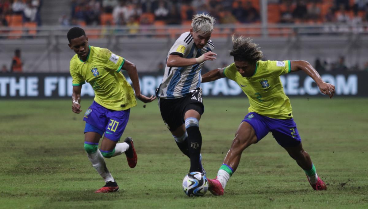 Pemain Argentina, Ian Subiabre  melepaskan diri dan melewati penjagaan dua pemain Brasil pada laga babak 8 besar Piala Dunia U-17 2023 di Stadion JIS, Jumat (24/11/23). - INDOSPORT