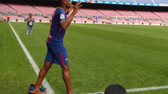 Yerry Mina melepas sepatunya saat pertama kali menginjak rumput Stadion Camp Nou. Copyright: © Getty Images