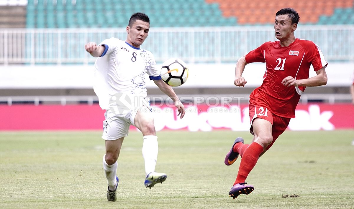 Pemain Uzbekistan, Kenjabaev Islom (kiri) memcoba melewati pemain Korut, Kim Nam II. Herry Ibrahim/INDOSPORT. Copyright: © Herry Ibrahim/INDOSPORT