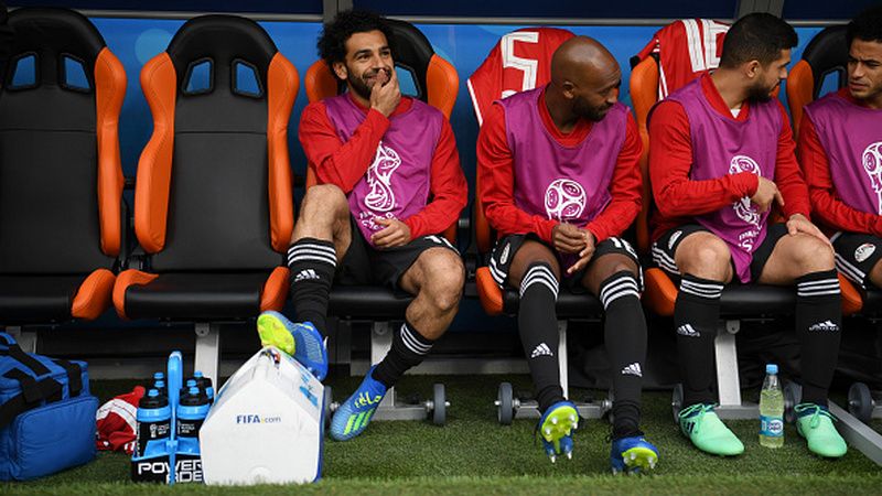 Mohamed Salah (kiri) duduk di bangku cadangan Mesir dalam pertandingan melawan Uruguay. Copyright: © Getty Images