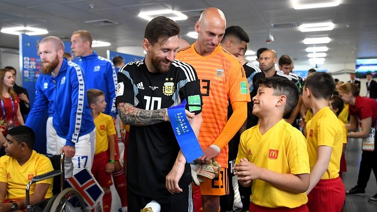 Kapten Argentina, Lionel Messi, berbicara dengan bocah maskot pertandingan di dalam lorong stadion jelang laga perdana Grup D Piala Dunia 2018 menghadapi Islandia. Copyright: © fifa.com