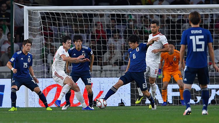 Wataru Endo (Jepang) membuang bola saat pemain Iran berusaha membobol gawang Jepang. Copyright: © Getty Images