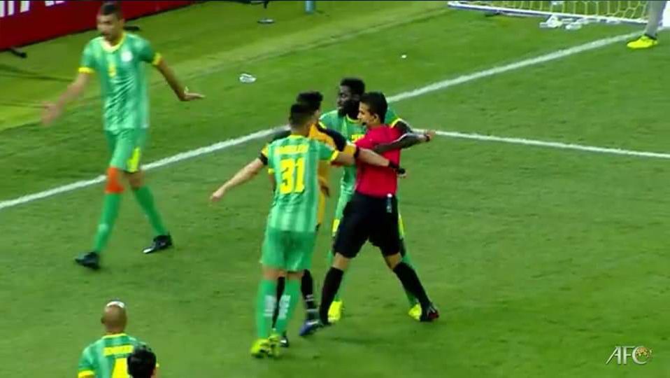 Wasit Thoriq Alkatiri diprotes pemain saat memutuskan hukuman penalti (di luar garis kotak penalti) di pertandingan Al-Makiya vs Al-Qadsia AFC Cup 2019. Copyright: © Twitter@MafiaWasit