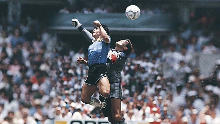 Diego Maradona (kiri) menggunakan tangannya untuk mencetak gol pertama saat melawan Inggris di perempatfinal Piala Dunia 1986. Copyright: © El Grafico/Getty Images