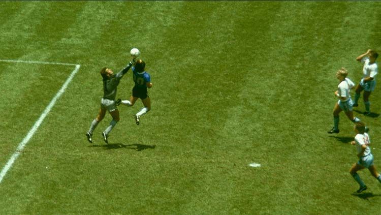 Diego Maradona (kanan) melompat dan menggunakan tangannya untuk mencetak gol pertama saat melawan Inggris di perempat final Piala Dunia 1986.  Copyright: © El Grafico/Getty Images