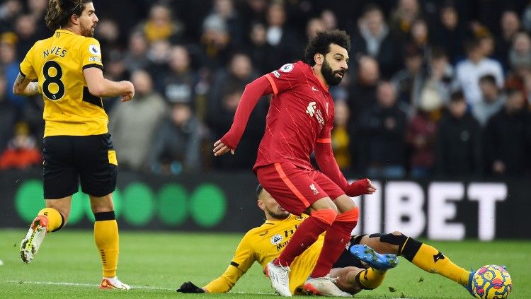 Mohamed Salah berduel dengan Romain Saiss memperebutkan bola di laga Wolves vs Liverpoo (04/12/21). Copyright: © REUTERS/Peter Powell