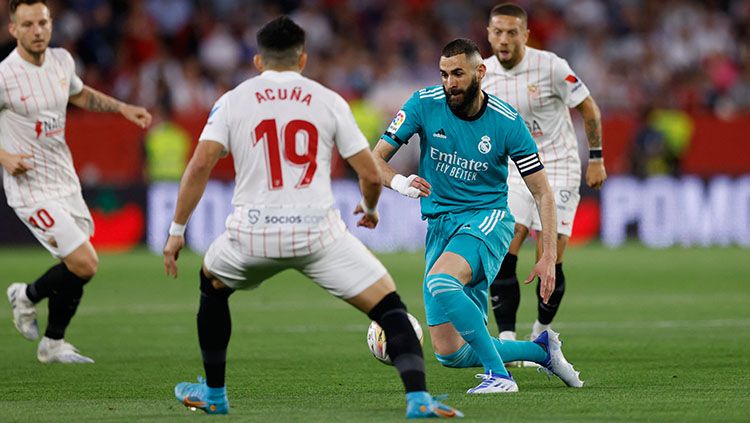 Pemain Real Madrid, Karim Benzema, berusaha untuk melewati adangan pemain Sevilla di Liga Spanyol. Copyright: © REUTERS/Marcelo Del Pozo