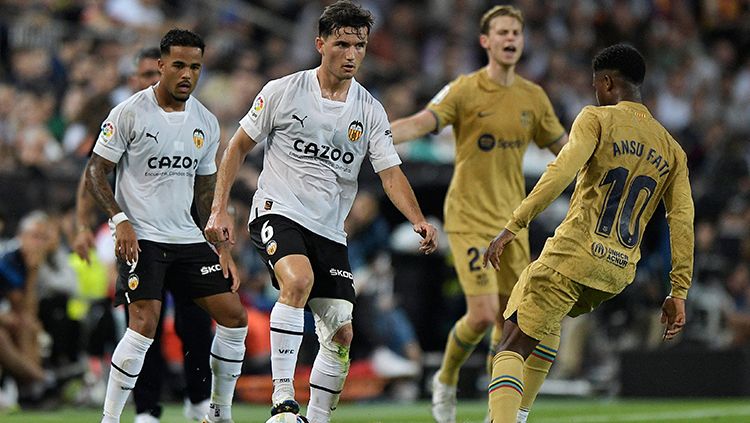 Pemain Valencia sedang diadang pemain Barcelona saat bentrok di Liga Spanyol. Copyright: © REUTERS/Pablo Morano