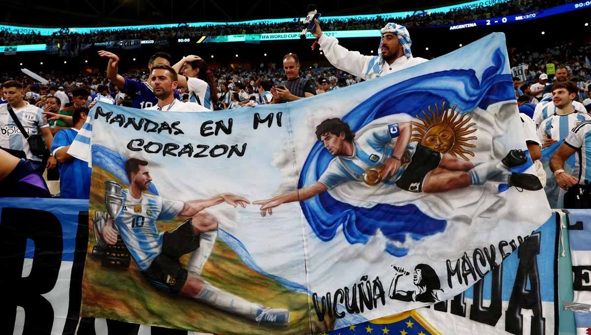 Suporter Argentina merayakan kemenangan dengan spanduk bergambar Lionel Messi dan Diego Maradona Piala Dunia Qatar 2022. (Foto: REUTERS/Pedro Nunes) Copyright: © REUTERS/Pedro Nunes