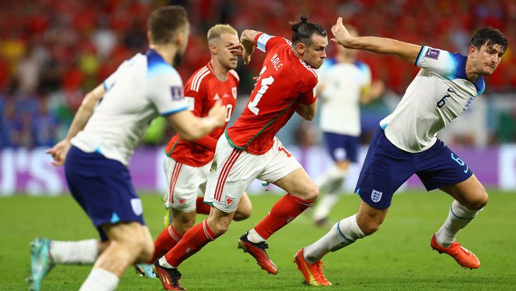 Laju striker Timnas Wales, Gareth Bale (tengah) ditahan oleh bek tengah Timnas Inggris, Harry Maguire (kanan) dalam pertandingan Grup B Piala Dunia 2022 (Foto: REUTERS/Hannah Mckay). Copyright: © REUTERS/Hannah Mckay