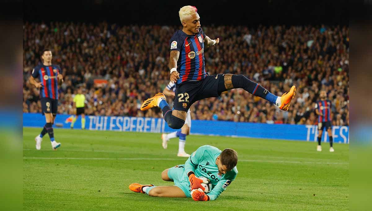 Pemain Barcelona, Raphinha lakukan aksi terbang hindari bentrok dengan pemain Real Sociedad, Alex Remiro. (Foto: REUTERS/Albert Gea) Copyright: © REUTERS/Albert Gea
